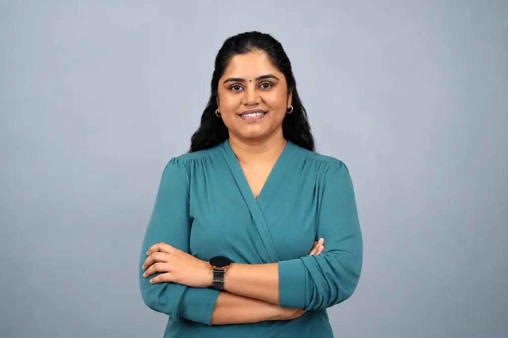 Revathi Varadarajalou in a teal top with arms folded, against a soft blue-grey backdrop
