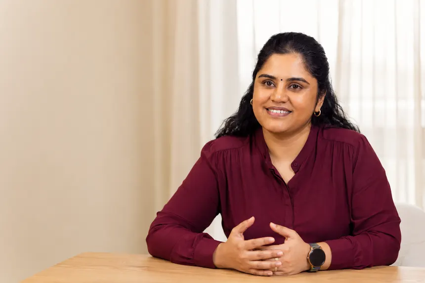 Revathi Varadarajalou seated at a table in a bright room, hands clasped, mid-conversation